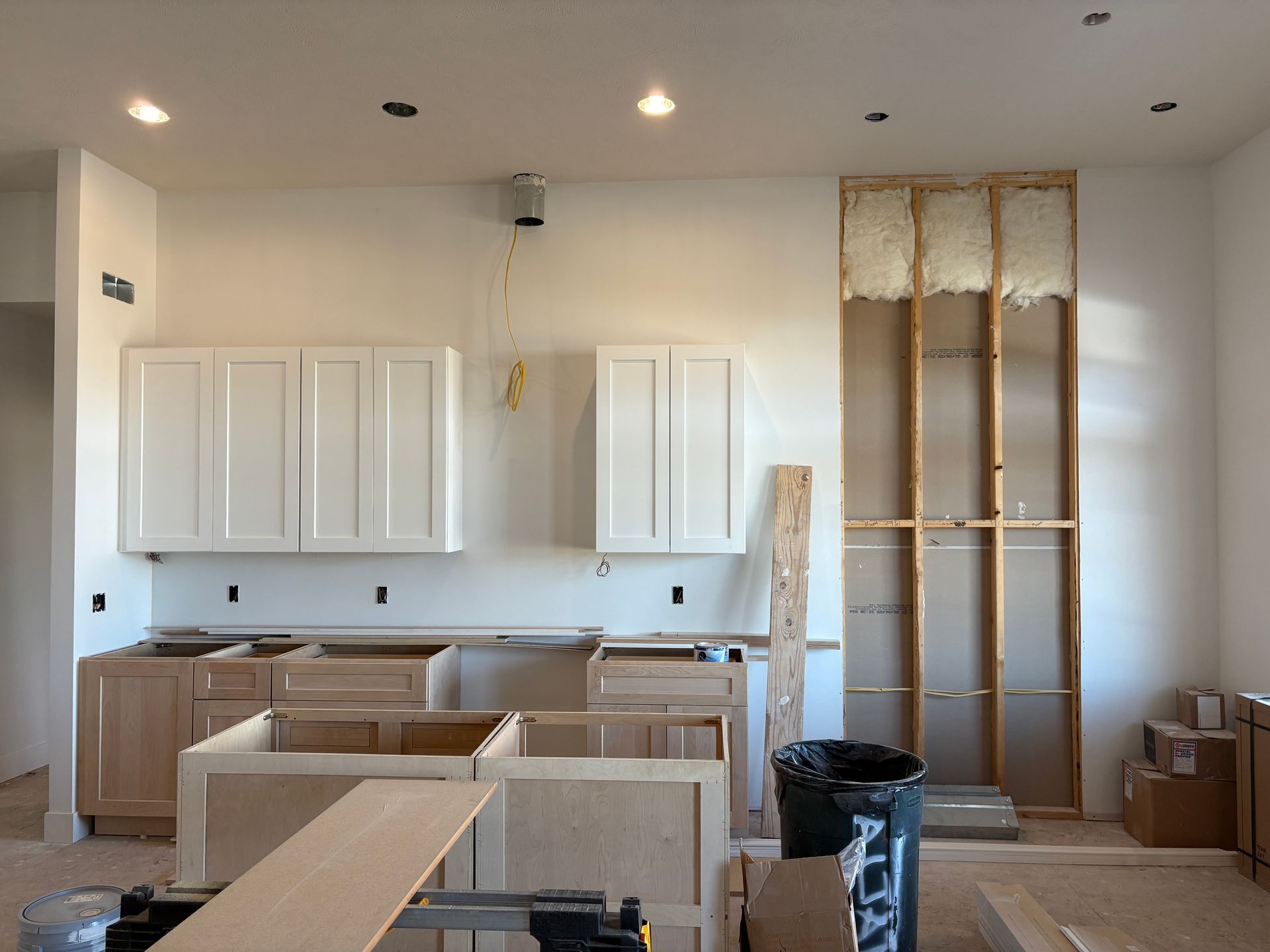 Kitchen renovation in progress, featuring unfinished cabinets, exposed wall framing, and recessed lighting.