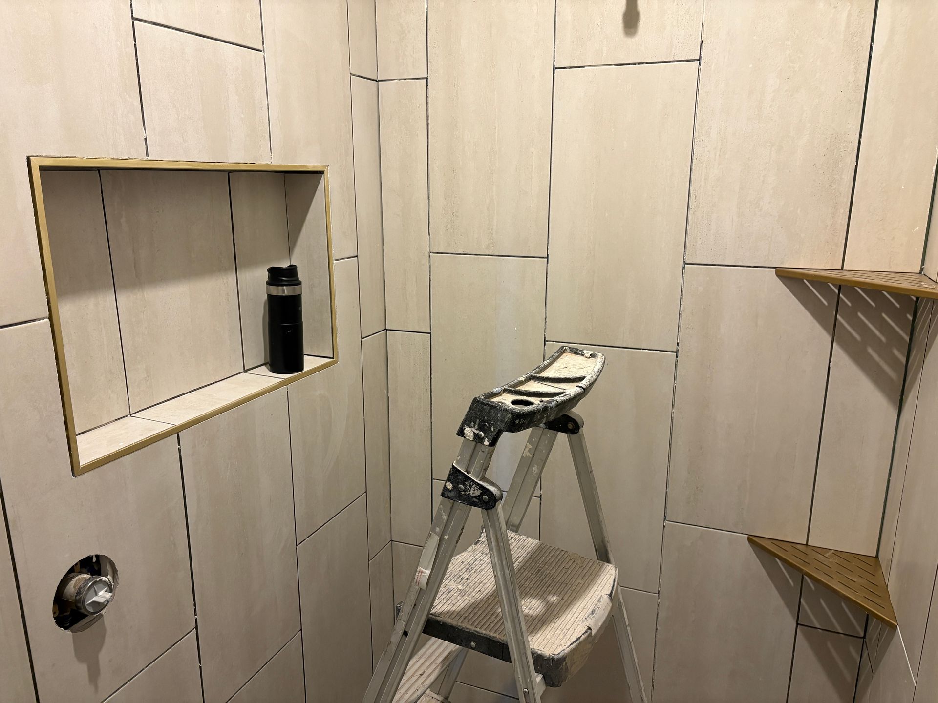 Shower stall with tiled walls, a built-in shelf, and a small step ladder inside.