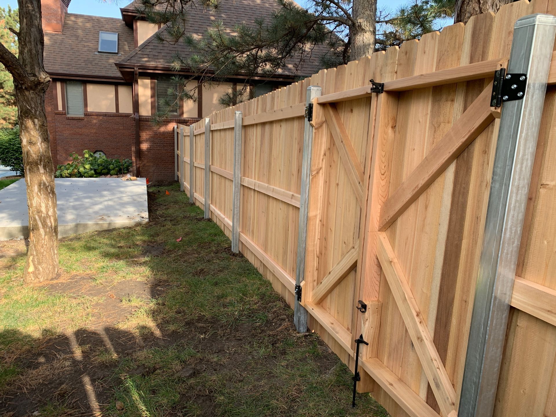 A wooden fence with a gate in a backyard. The fence is light-colored wood, with metal posts.