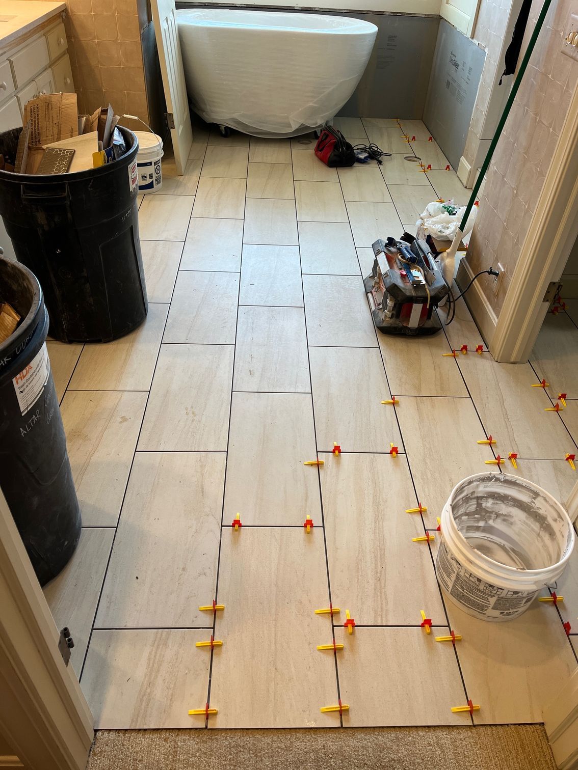 Bathroom floor tiled with light-colored rectangular tiles. Orange spacers are between the tiles.