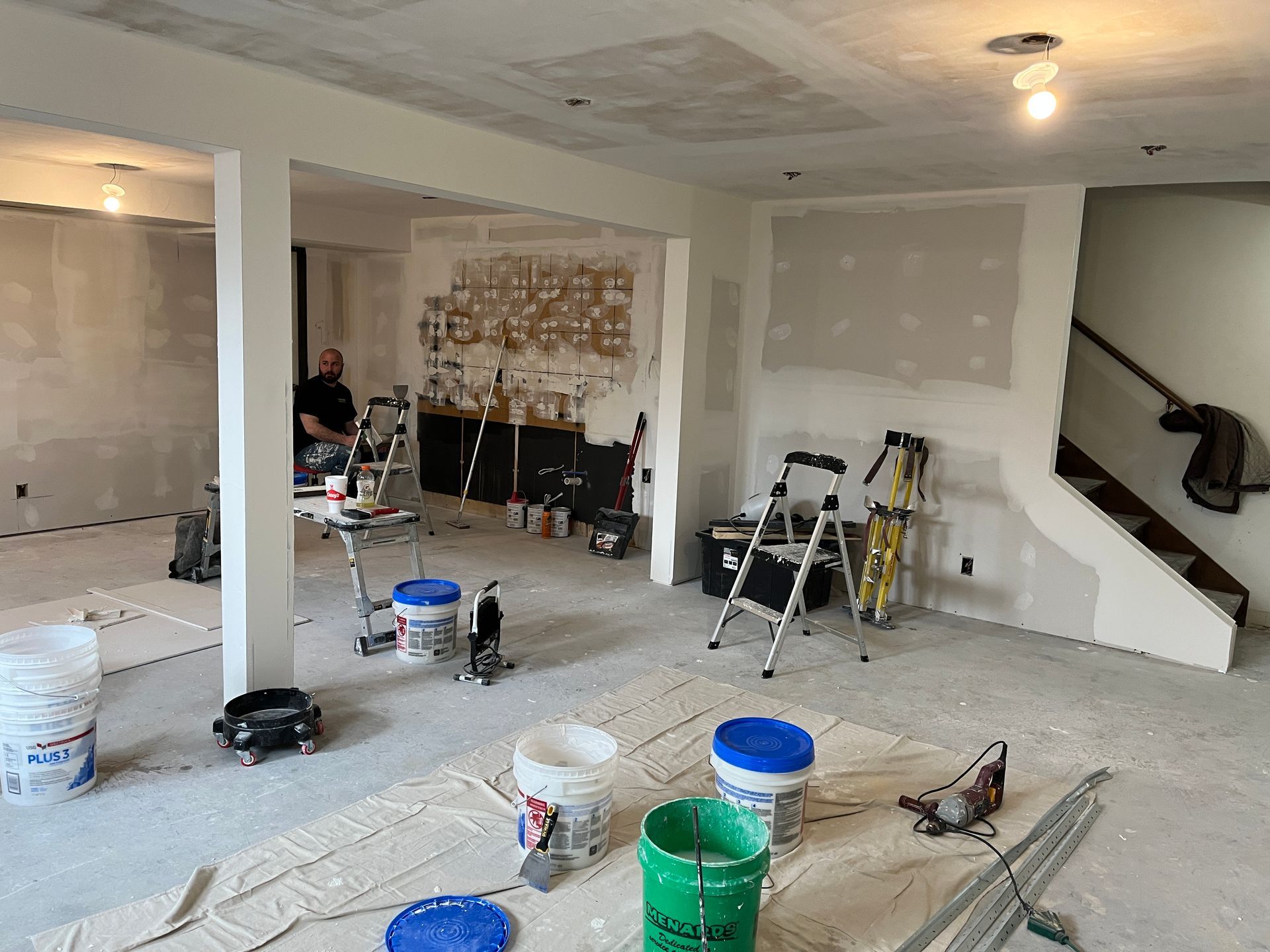 A man is standing in a room with buckets of paint and a ladder.
