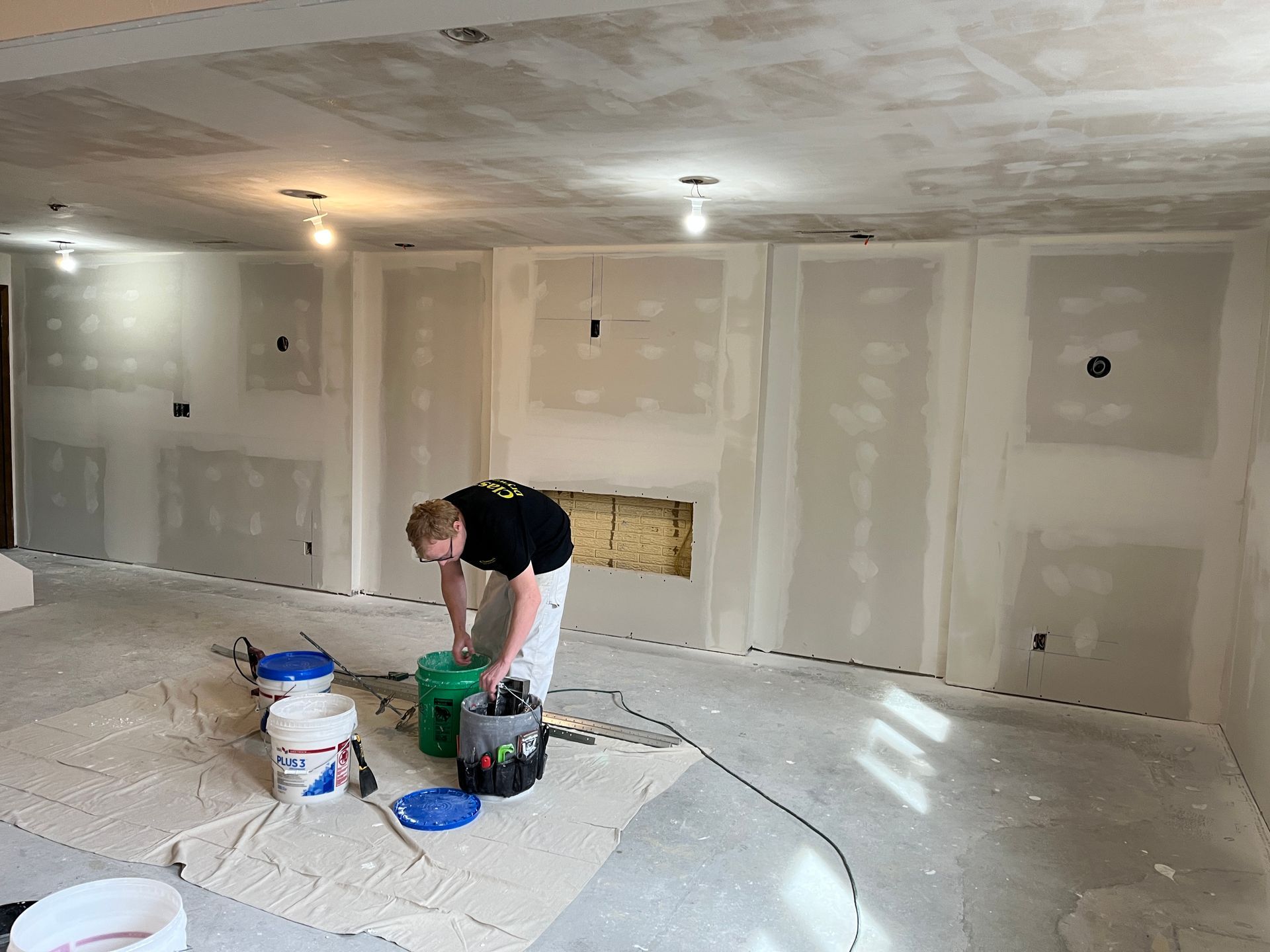 A man is kneeling down in a room with buckets of paint.