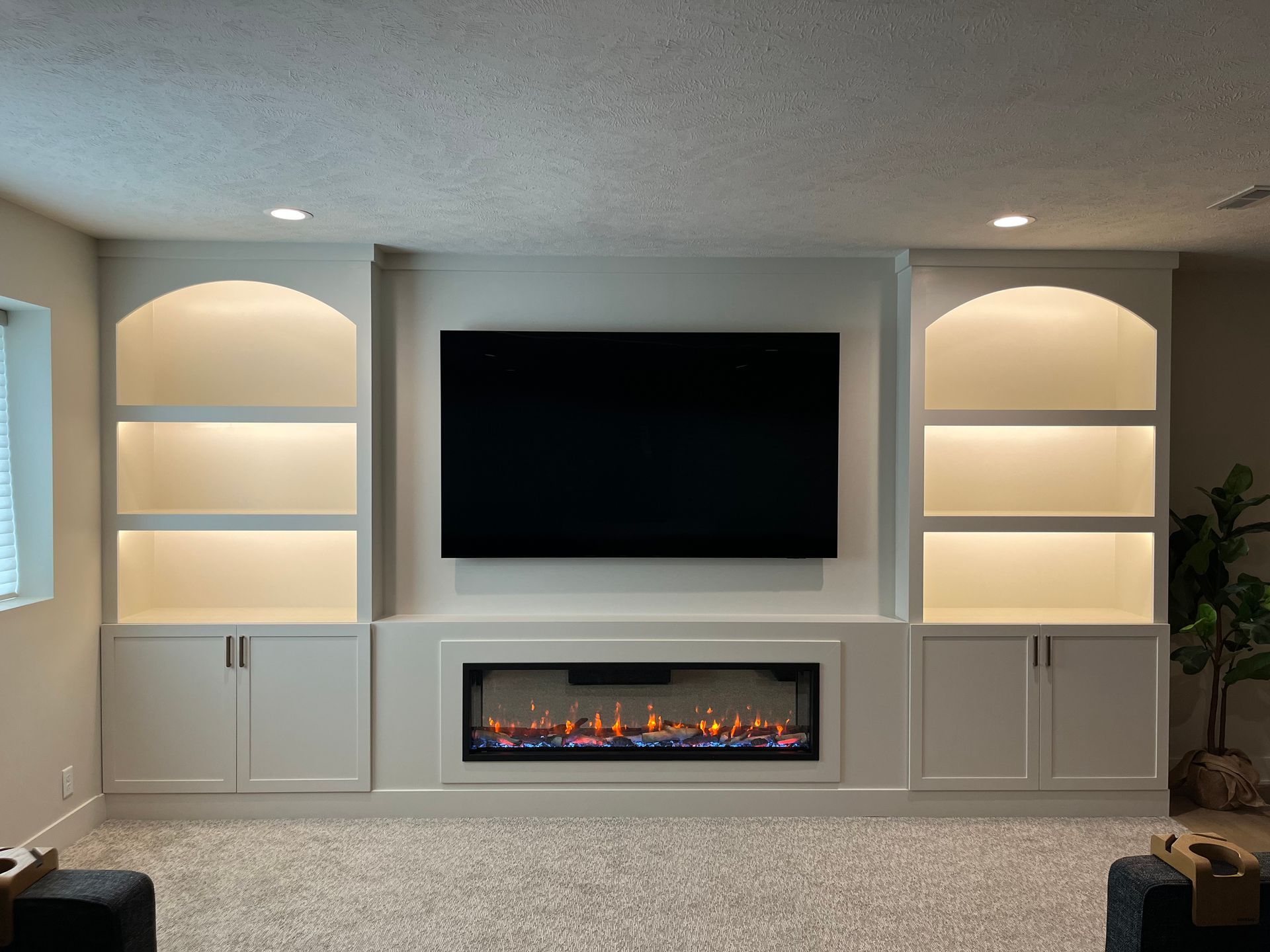 Built-in entertainment center with a fireplace, TV, and lit shelving, painted white.