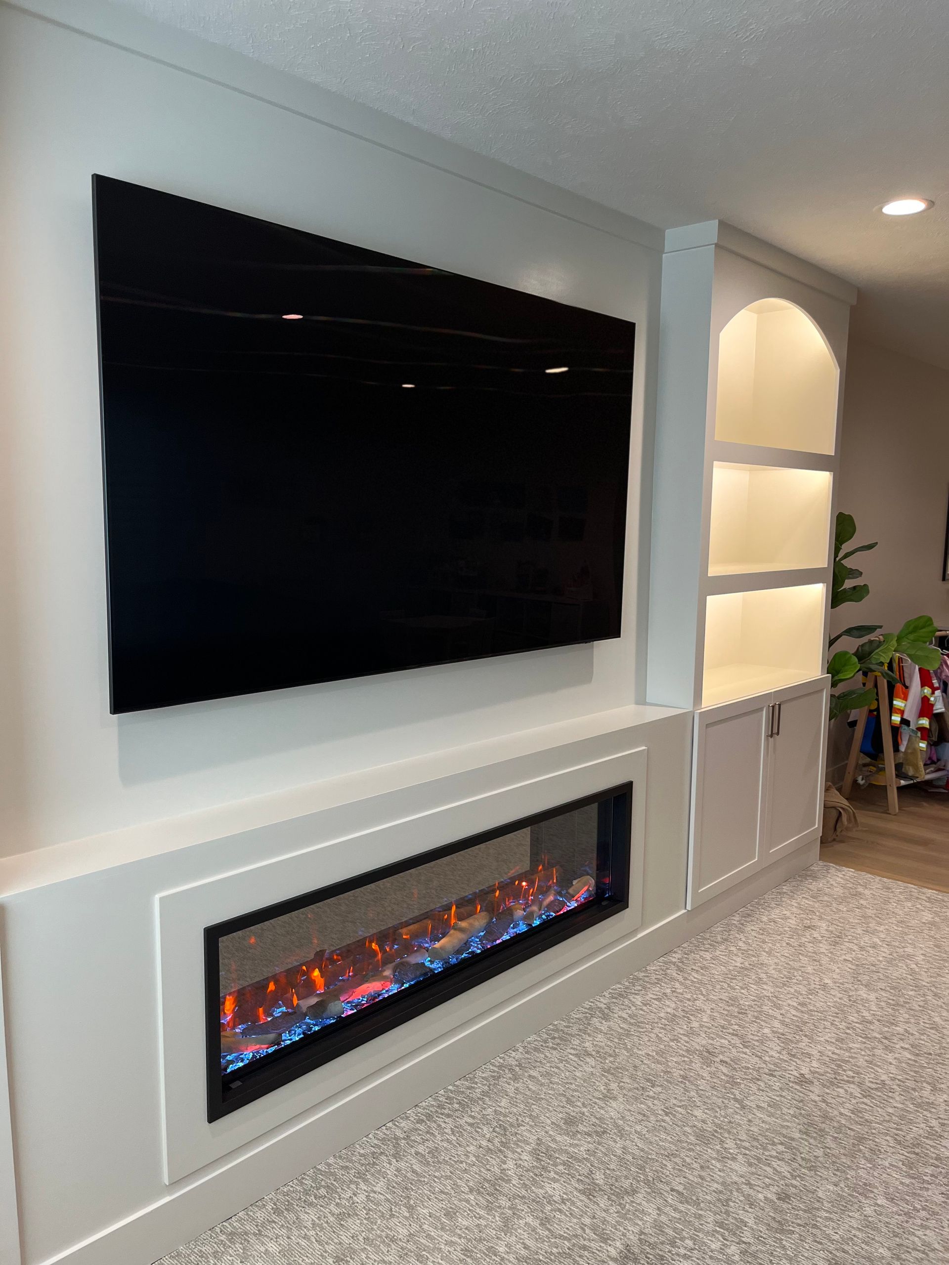 Wall-mounted TV above an electric fireplace, flanked by white built-in storage with a glowing light.