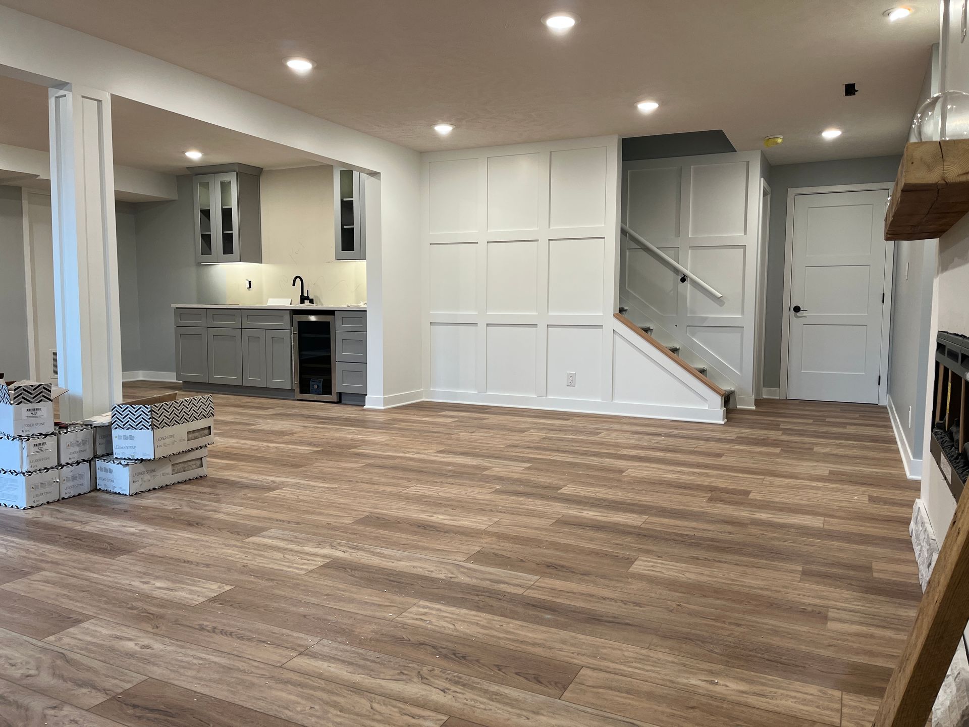 A basement with hardwood floors , stairs , a kitchen and a fireplace.