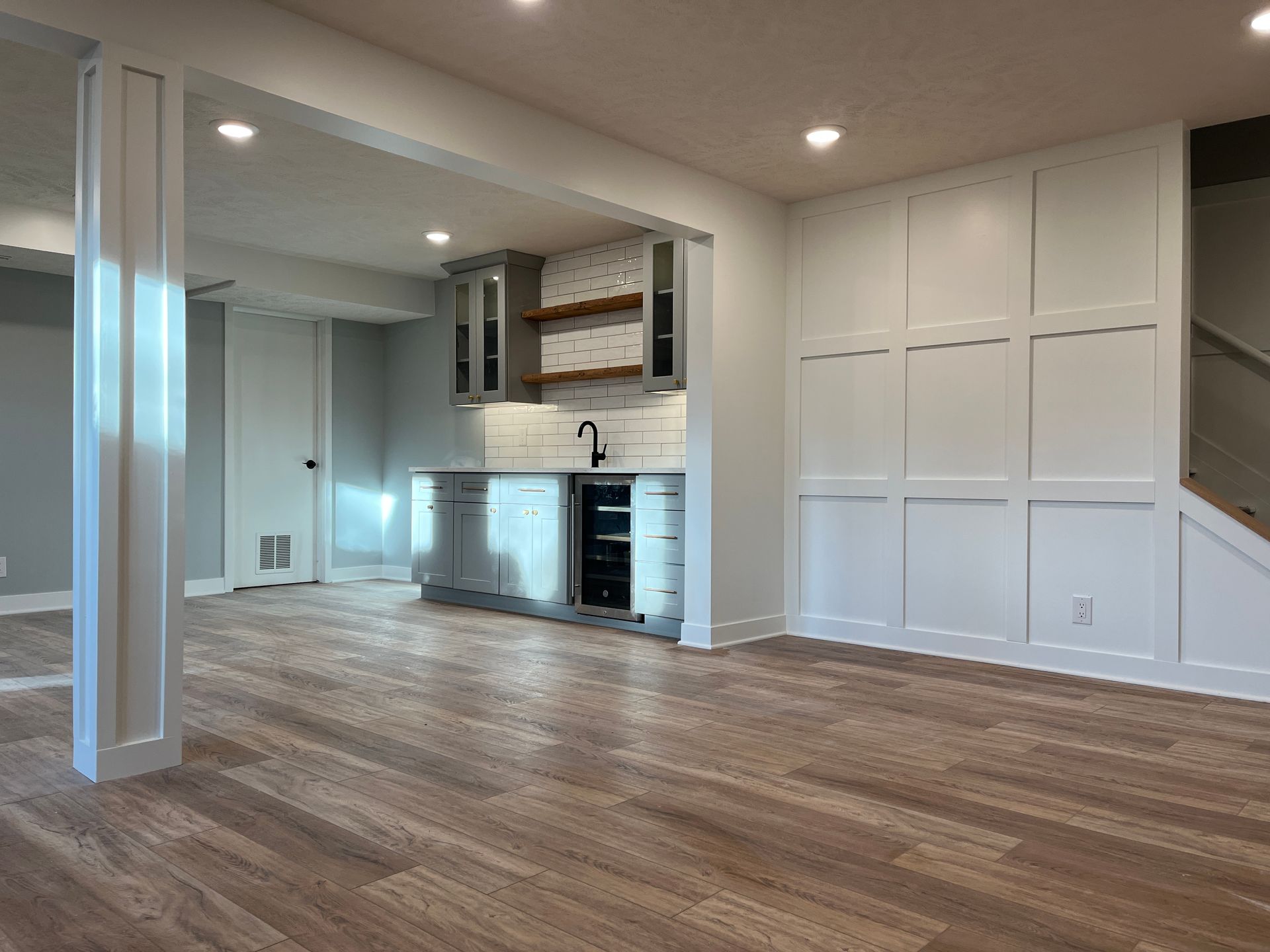 A living room with hardwood floors , white walls , and a kitchen.