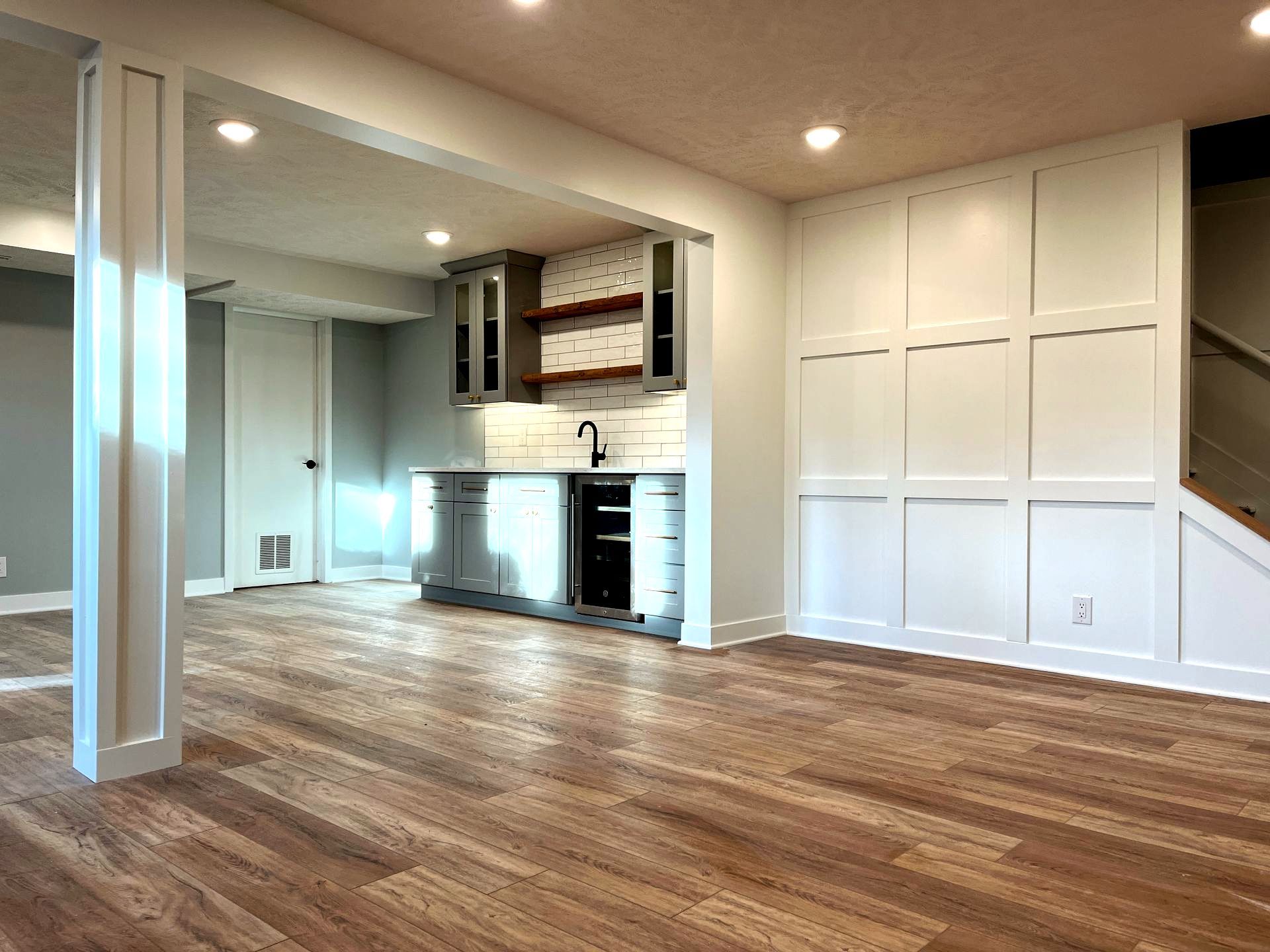 An empty basement with hardwood floors and a kitchen.