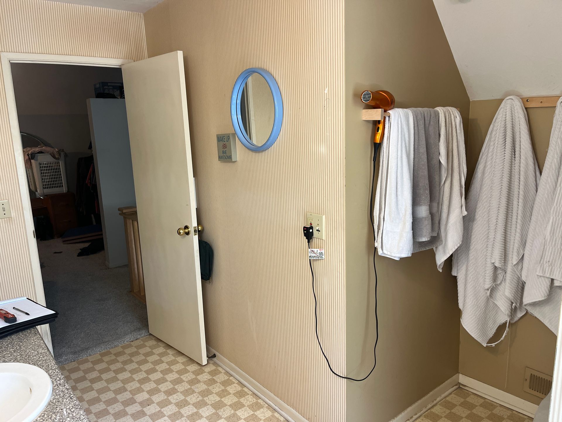Bathroom with beige and wavy patterned walls, open door, towels, mirror, and hairdryer.