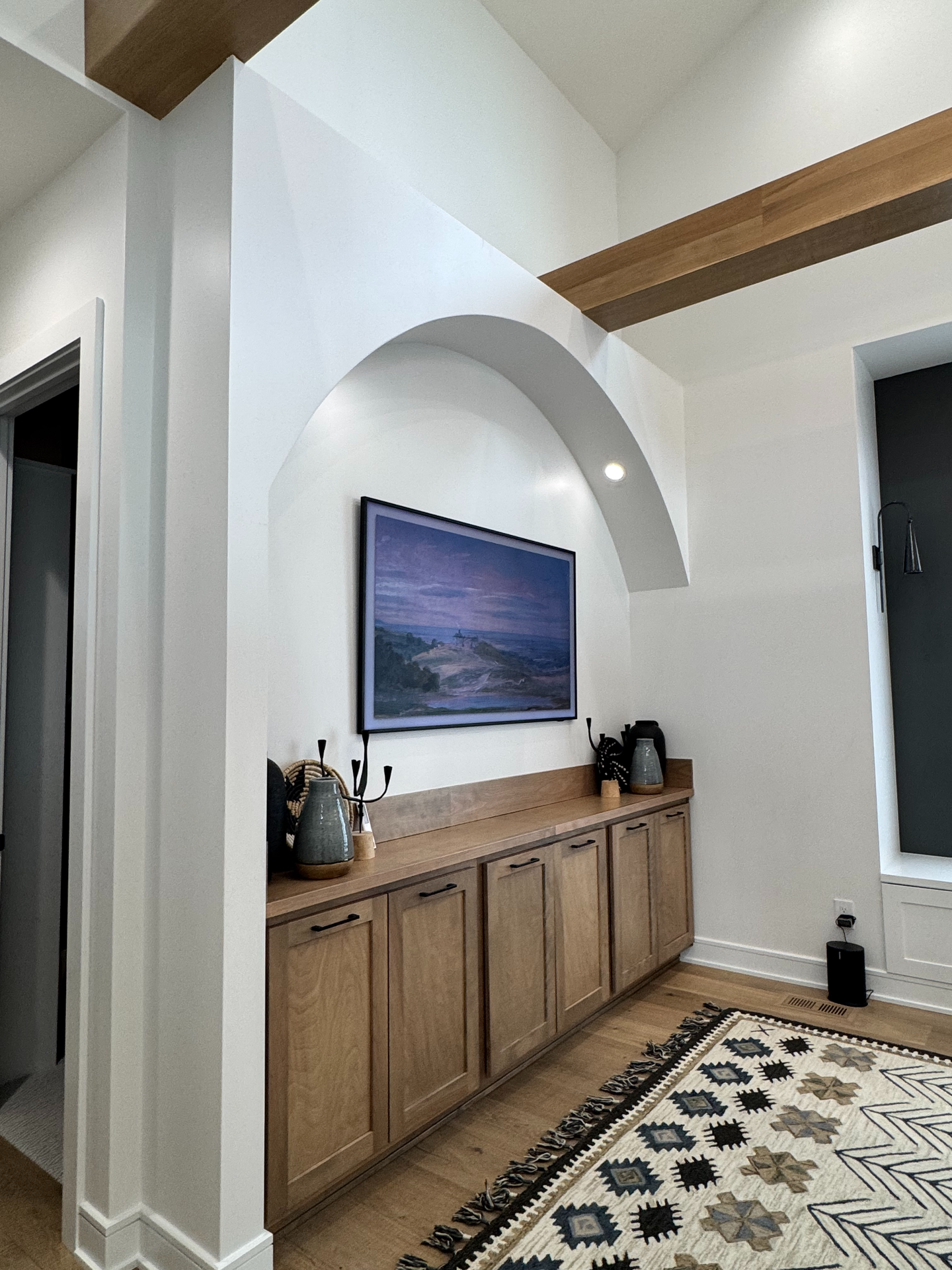 A living room with a tv on the wall and a rug on the floor.