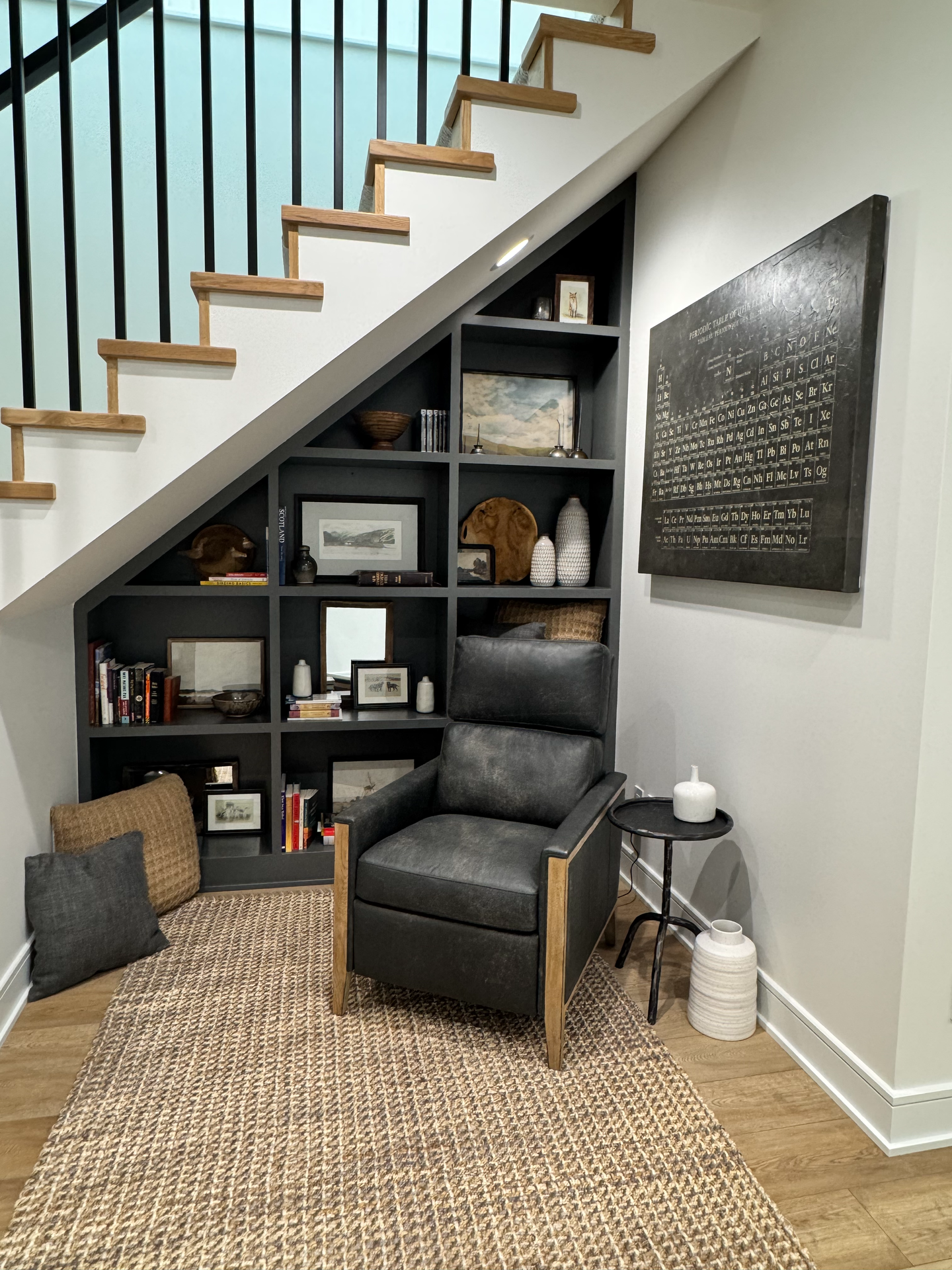 A living room with a chair and a bookshelf under the stairs.