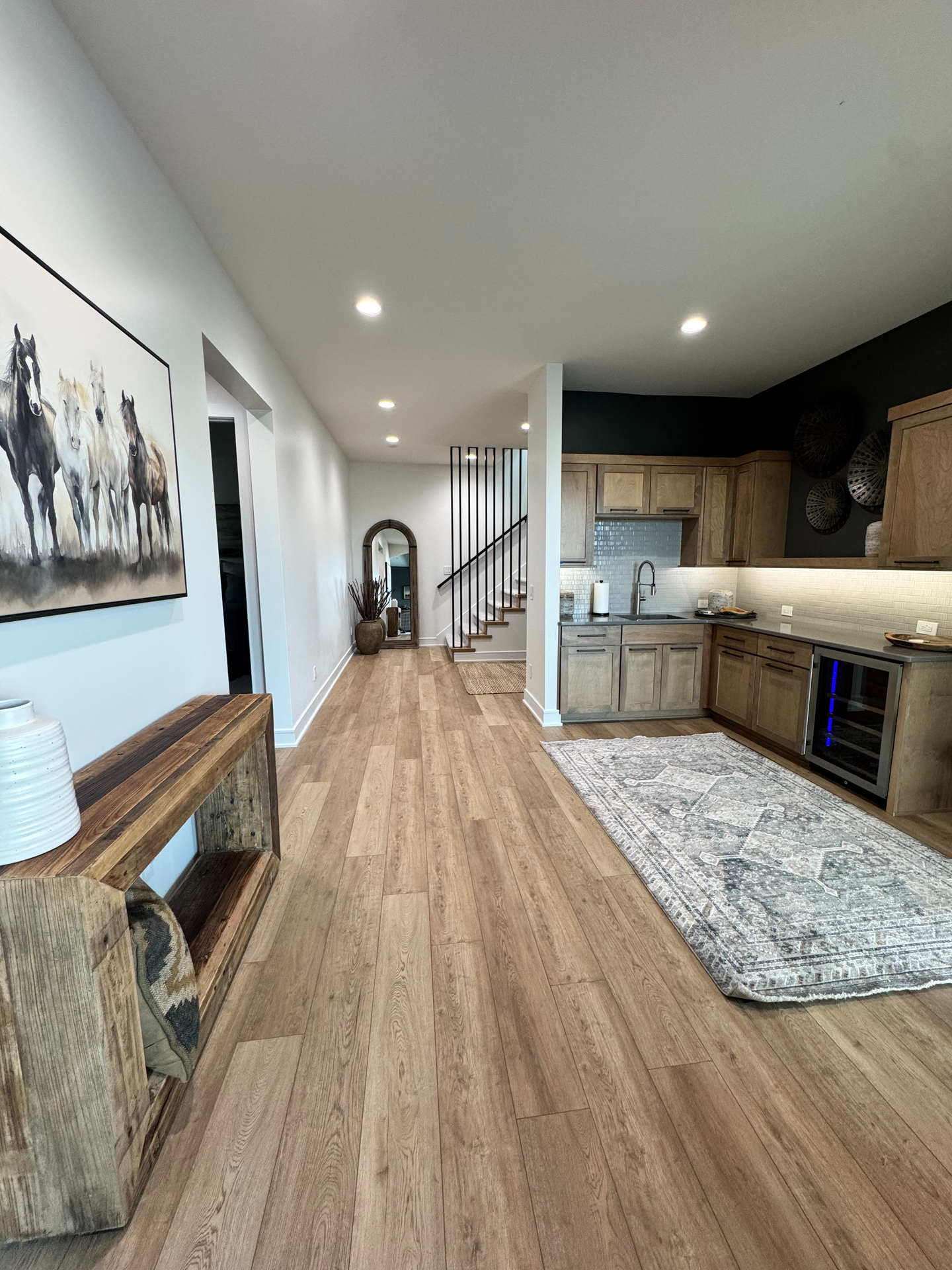 A hallway leading to a kitchen with hardwood floors and a painting of horses on the wall.