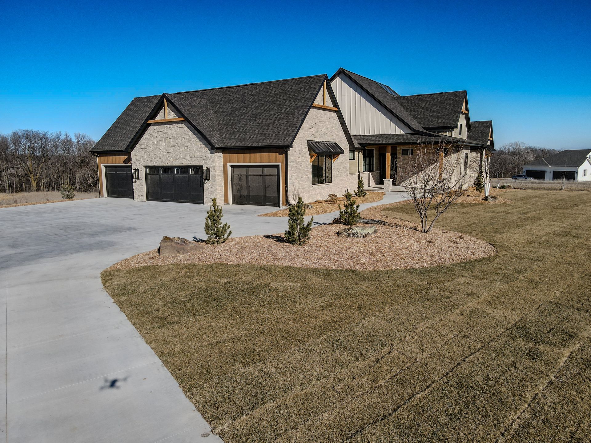 A large house with two garages and a driveway is sitting on top of a lush green field.