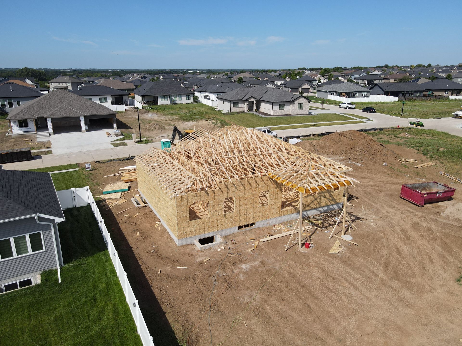 A house under construction with exposed wood framing, surrounded by other houses in a suburban setting.