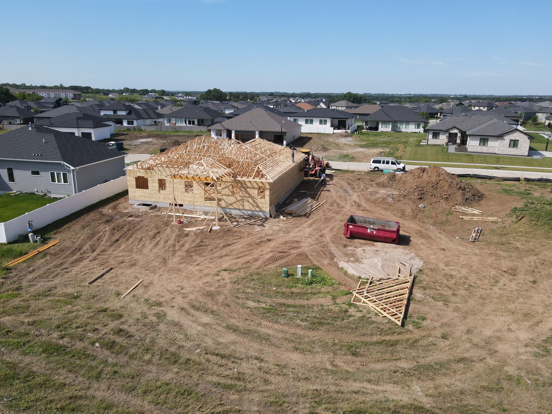Construction site with a house frame under construction; lumber, and other houses in the background under a blue sky.