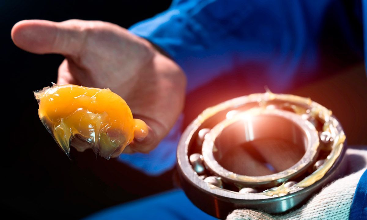 Mano sosteniendo un rodamiento de bolas recubierto con grasa amarilla.