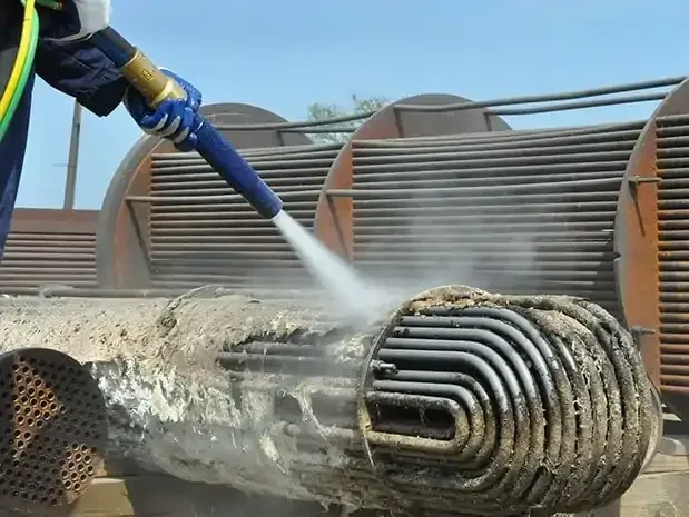 Persona que utiliza una manguera de agua para limpiar un intercambiador de calor, eliminando la suciedad y la mugre.