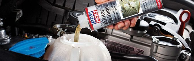 Una persona vierte líquido de un tubo en un recipiente blanco debajo del capó de un automóvil.