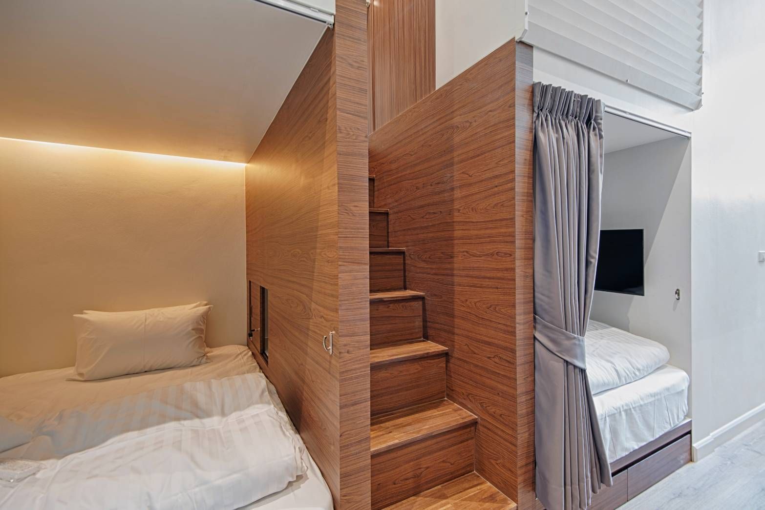 Modern room with built-in beds. Stairs lead to an elevated bed area. Brown and white tones throughout.