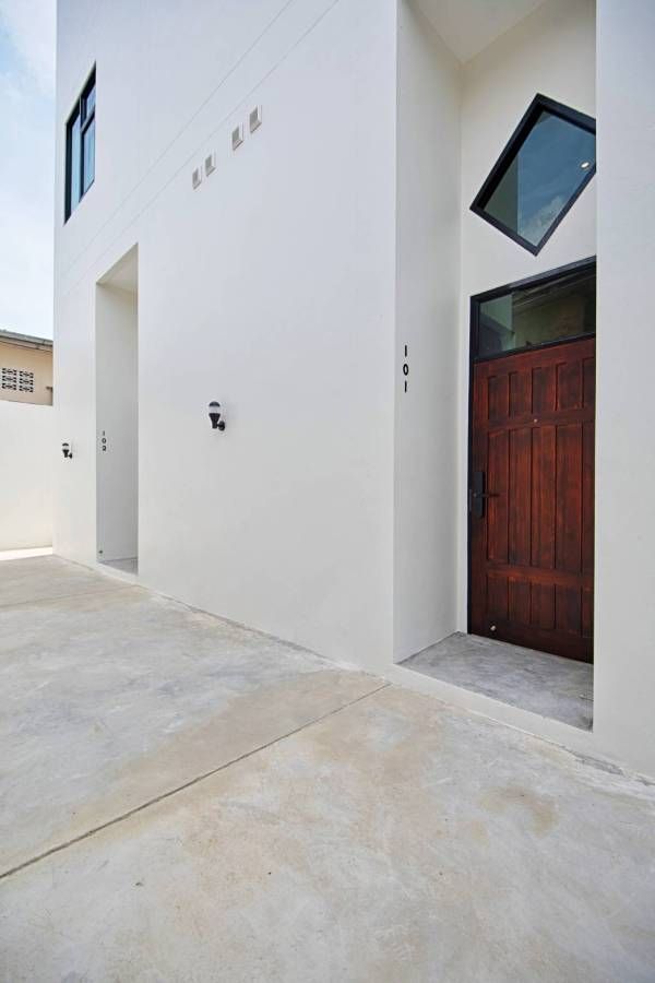 Exterior of modern white building with brown door and diamond-shaped window. Concrete patio.