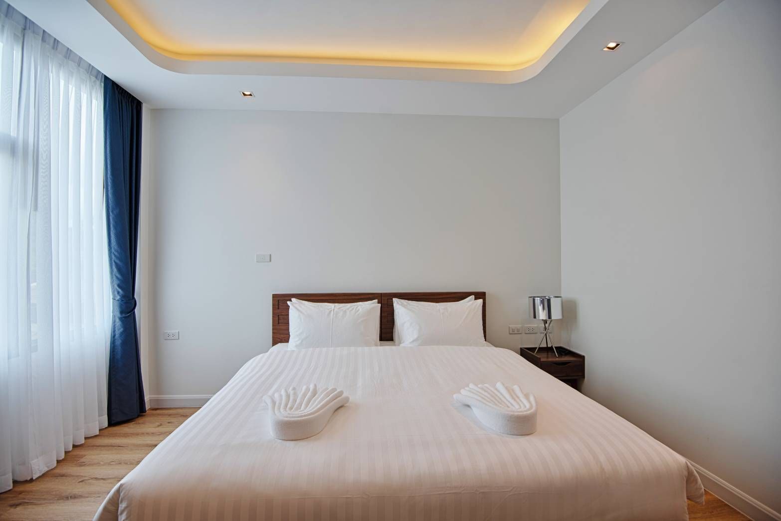Bedroom with a white bed, towels, bedside table, and curtains.