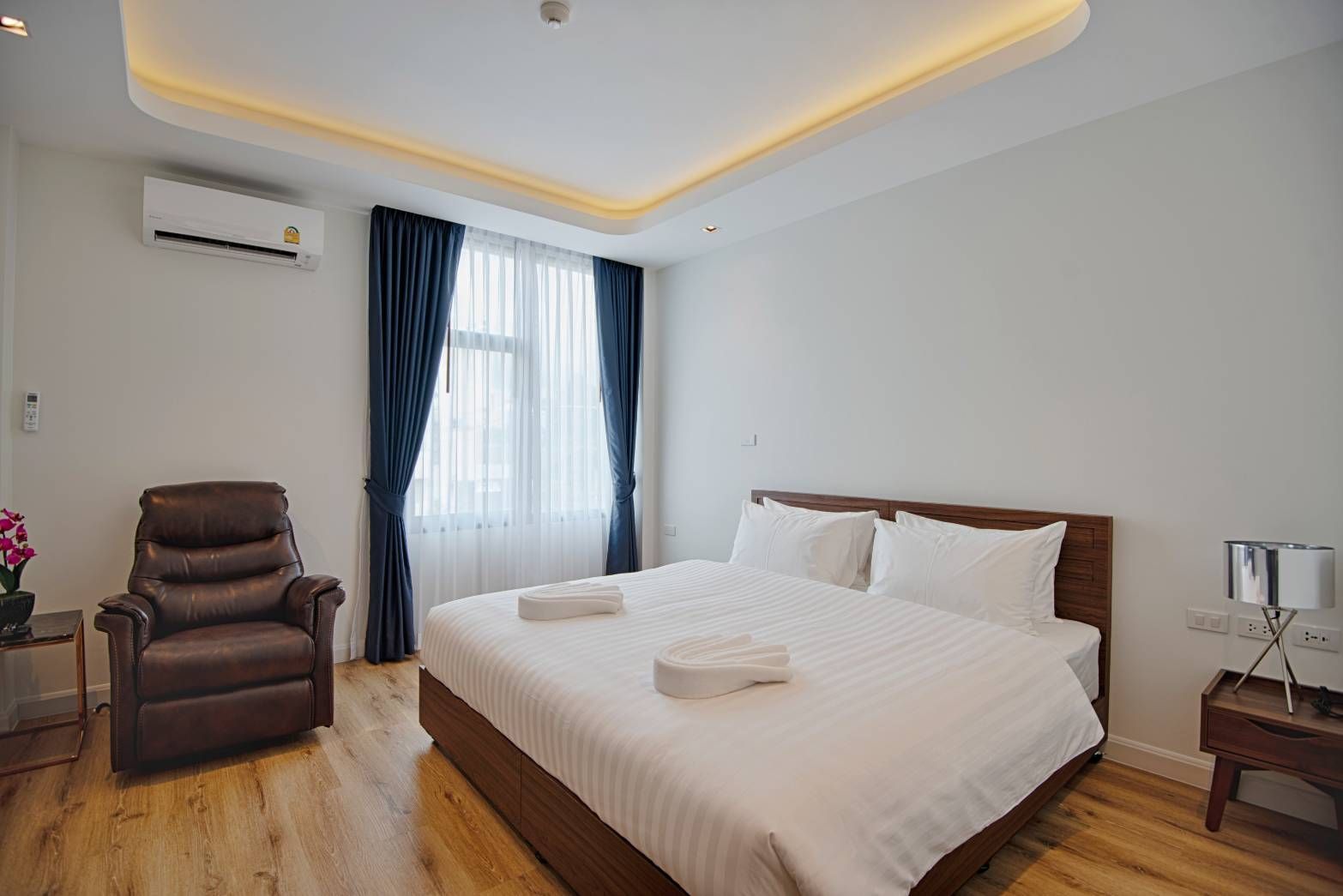 Bedroom with bed, armchair, window, air conditioner, and side table.