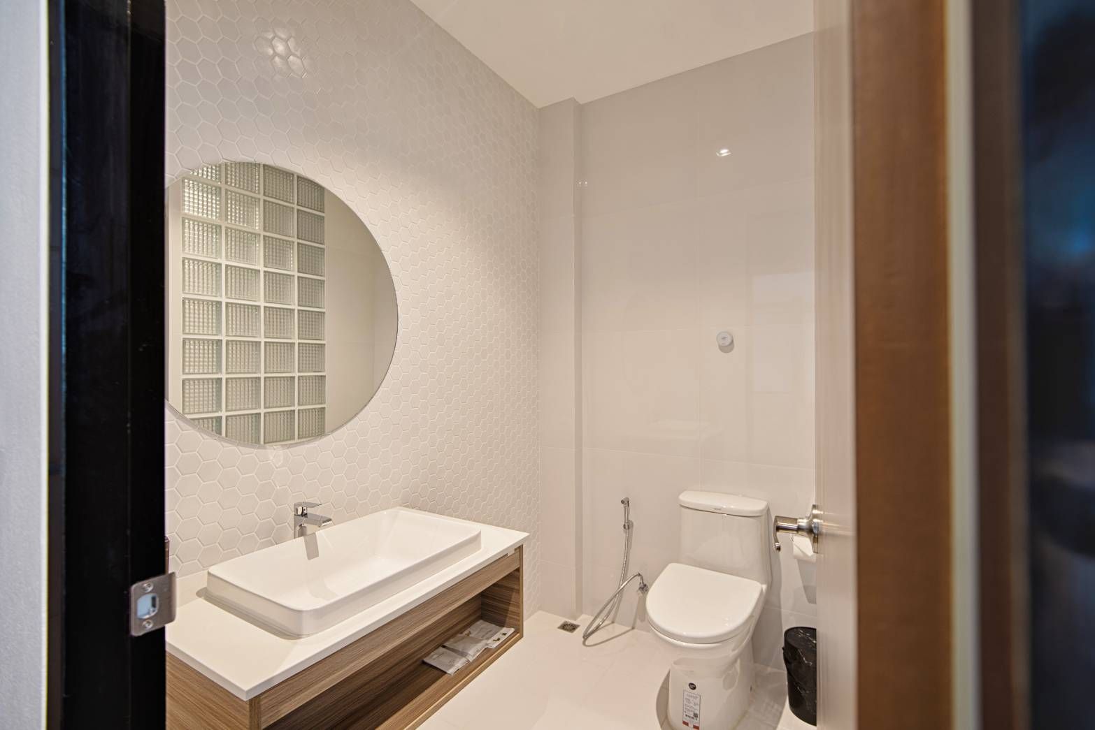 Modern bathroom with white walls, a vessel sink, round mirror, and toilet.