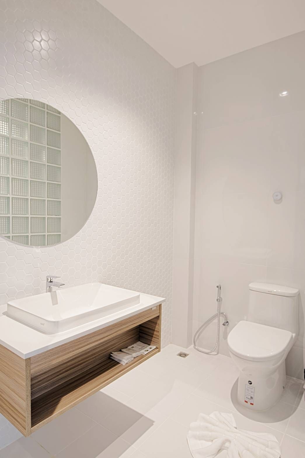 White bathroom with a rectangular sink on a wooden cabinet, a round mirror, and a toilet.
