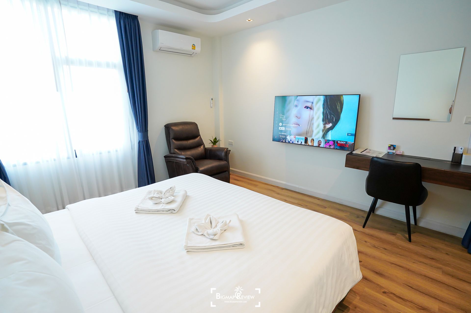 Hotel room with a bed, desk, armchair, and mounted TV.