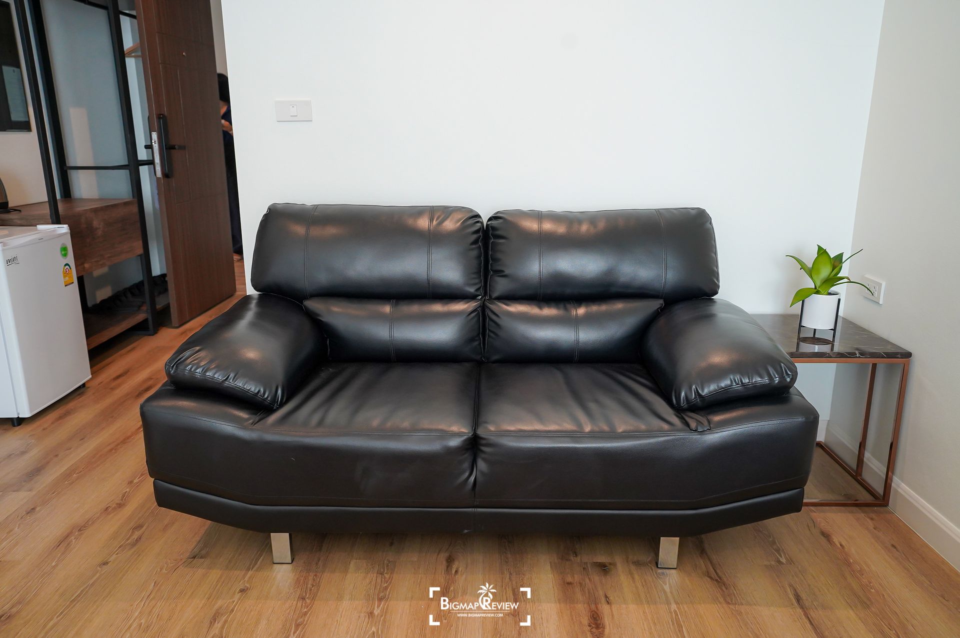 Black leather loveseat against a white wall in a room with wood flooring.