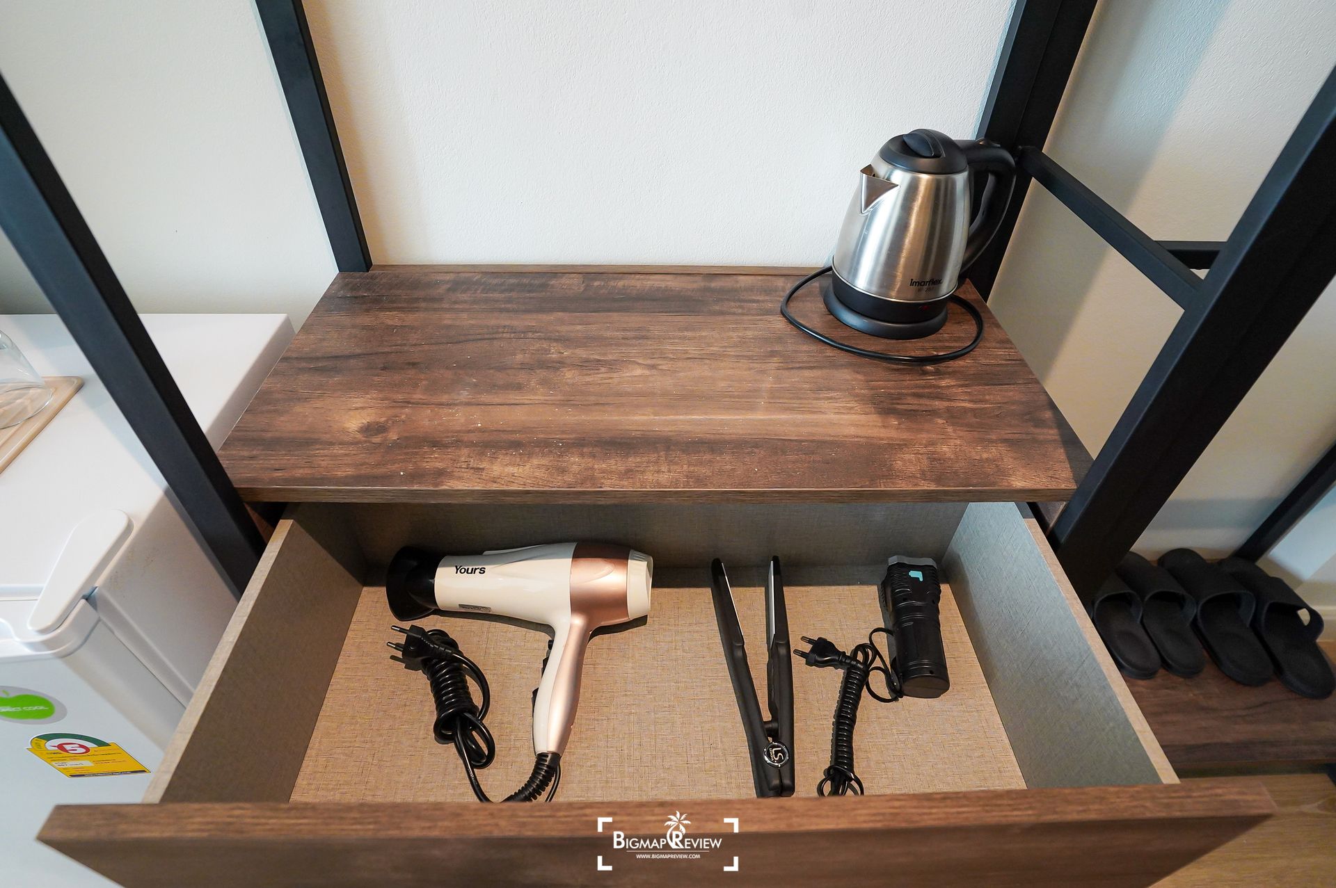 Shelf with a kettle, a hair dryer, a straightener, and other accessories in a drawer.