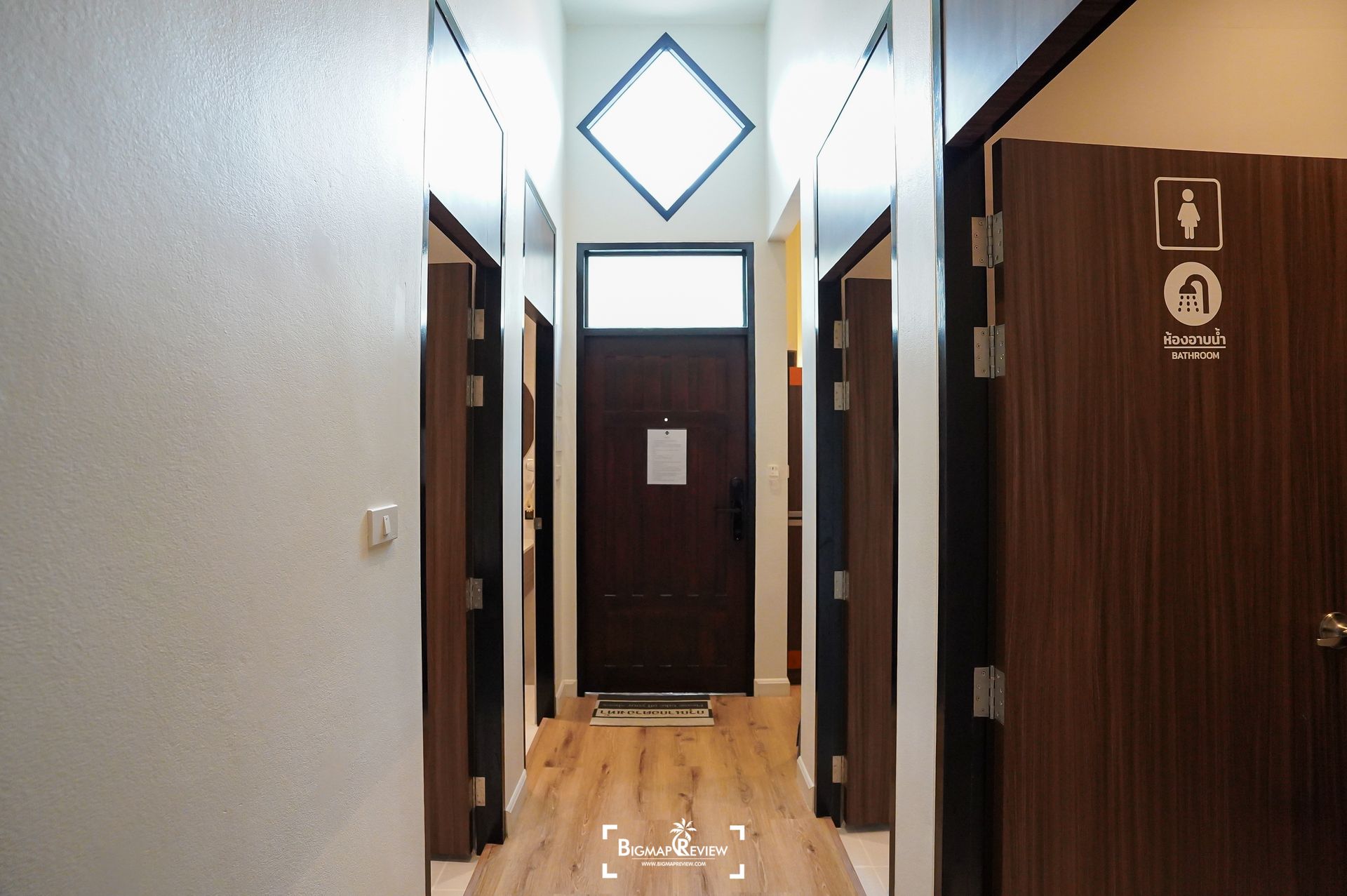 Hallway with doors, wooden floors, and a diamond-shaped window above a dark wood door.