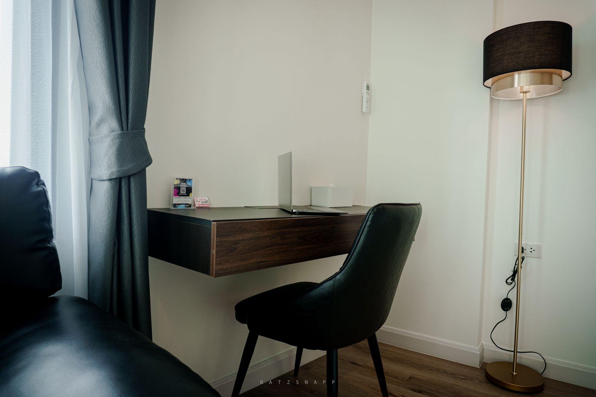 Workspace with floating desk, laptop, black chair, floor lamp, and window with gray curtains.