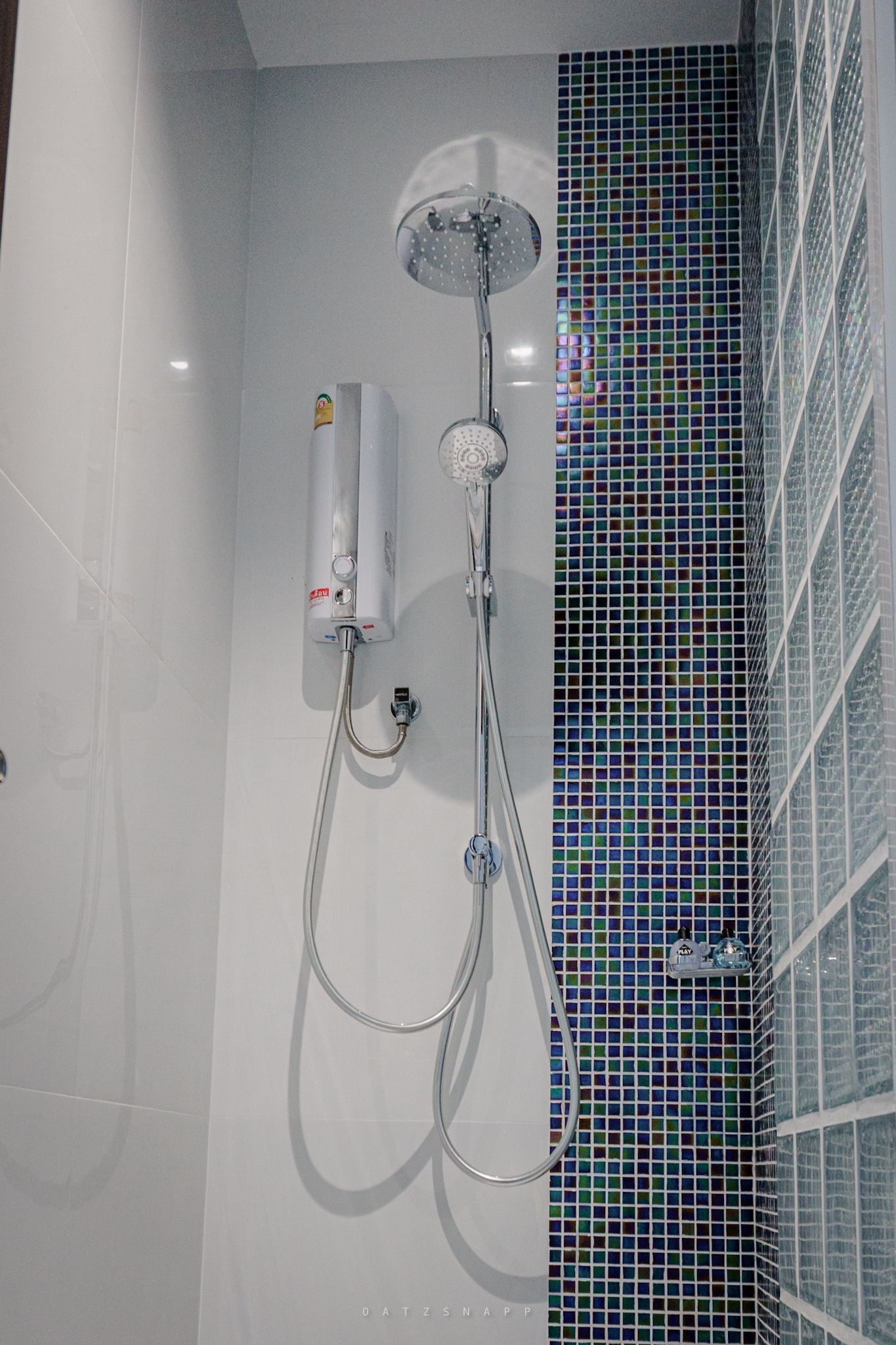 Shower with overhead rain showerhead, handheld shower, and water heater on tiled wall.