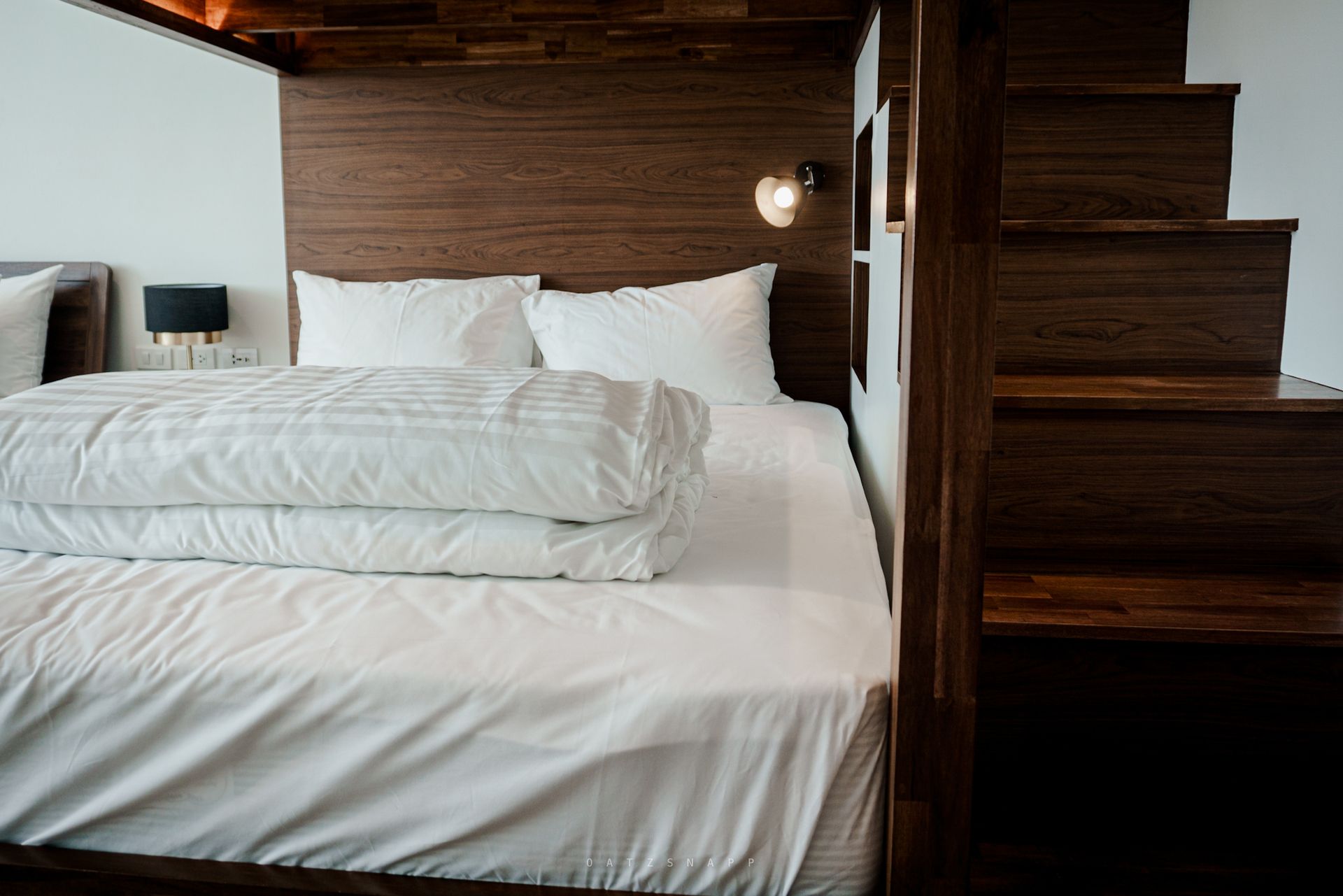 Bedroom with wooden headboard, white bedding, and stairs leading up.