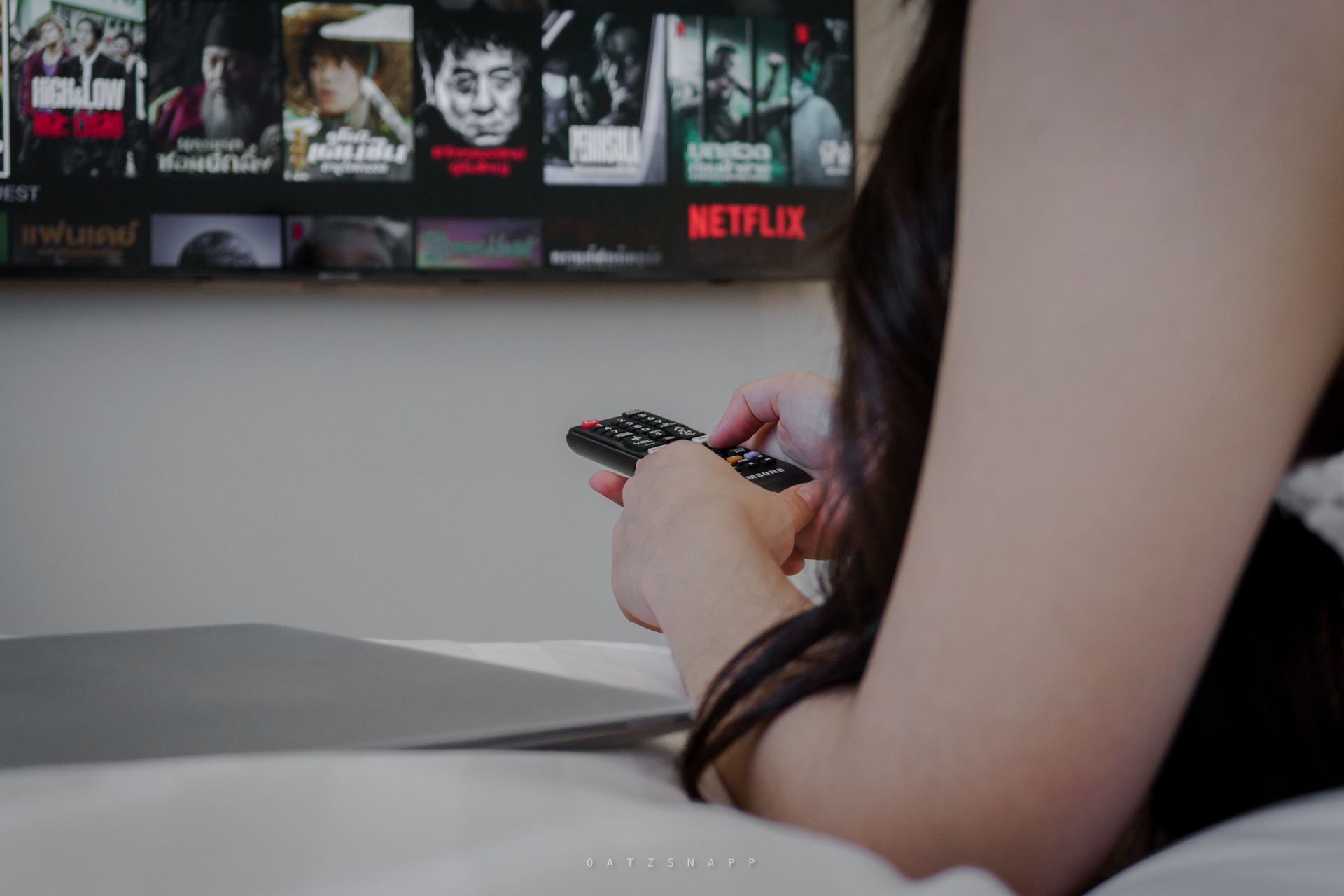 Person on a bed holding a remote, watching Netflix on a TV.