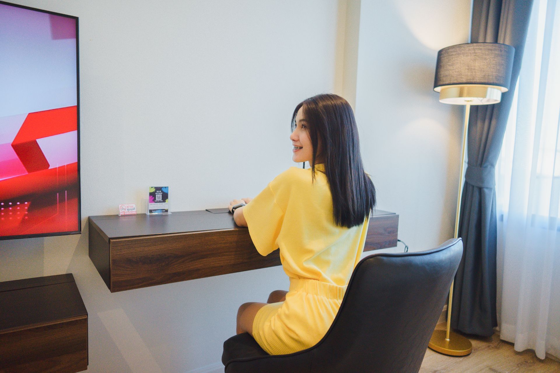 Woman in yellow outfit sits at a desk in a room.