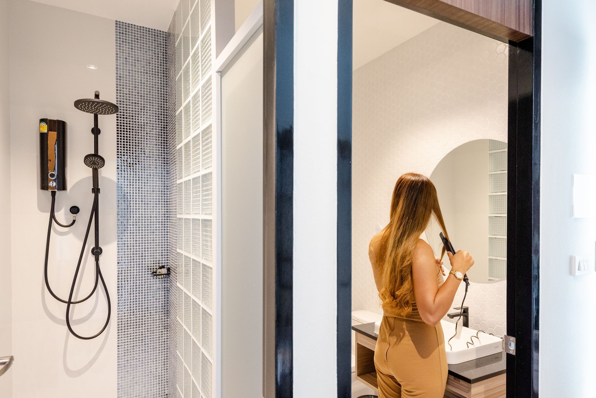 Woman styling her hair in bathroom, shower visible to the left.