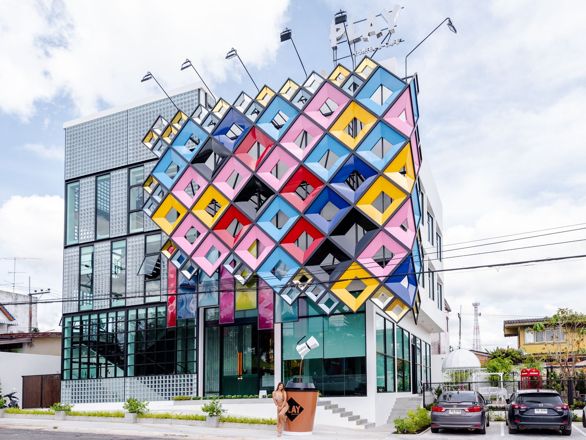 Colorful building facade with geometric diamond pattern. White, glass, and multi-colored cubes. Cars parked out front.