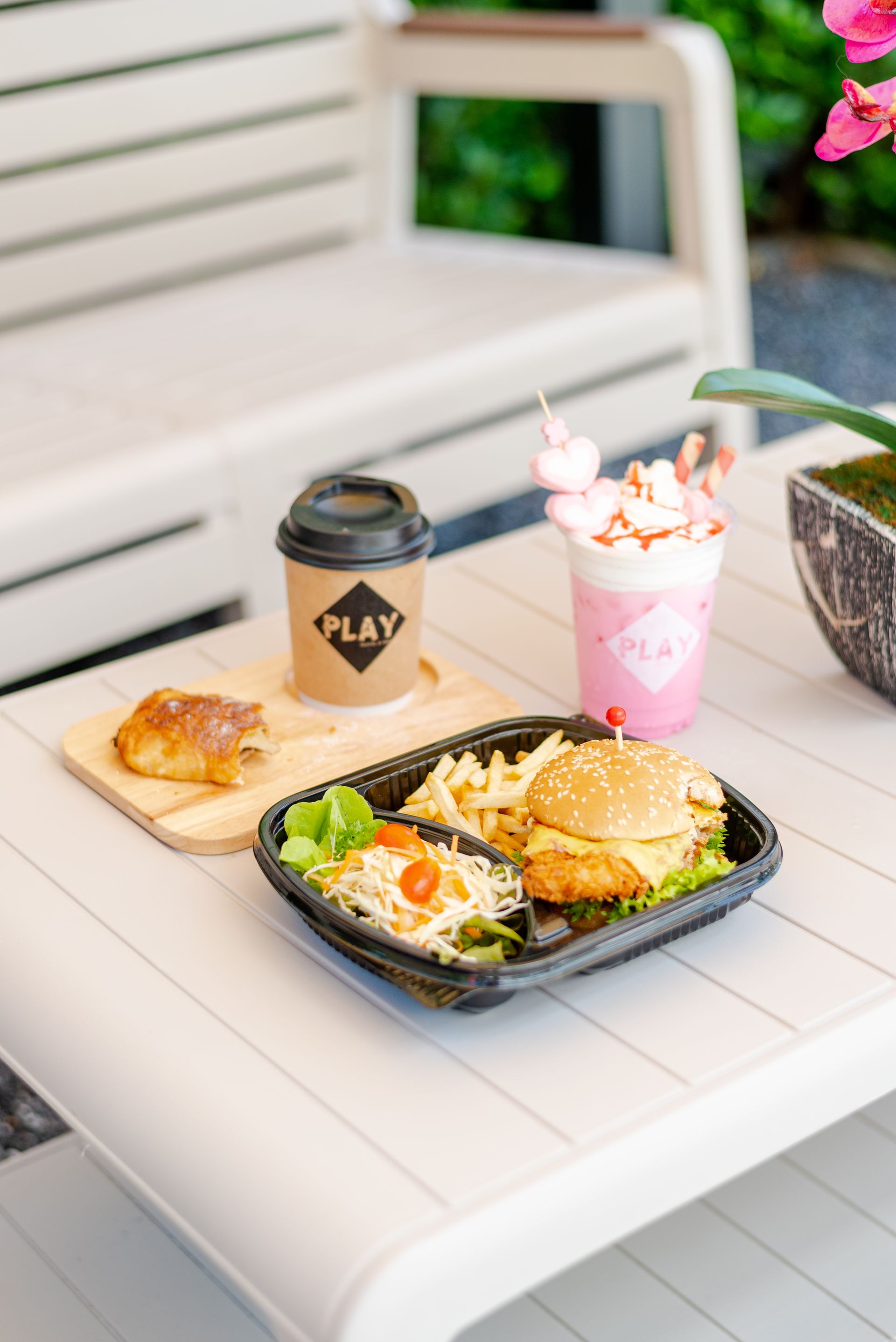 Table with food and drinks: burger, fries, salad, coffee, pink drink, croissant.