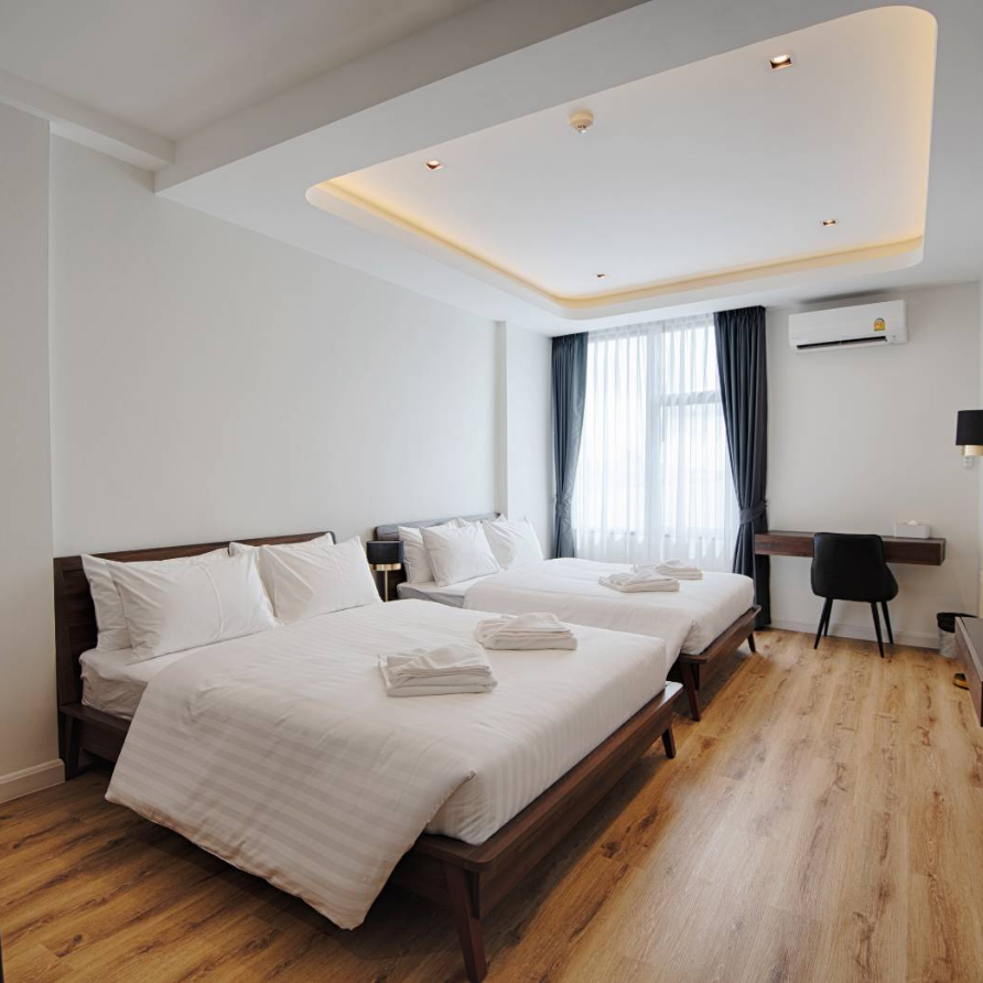 Hotel room with two double beds, white bedding, wooden floors, and a desk by a window.
