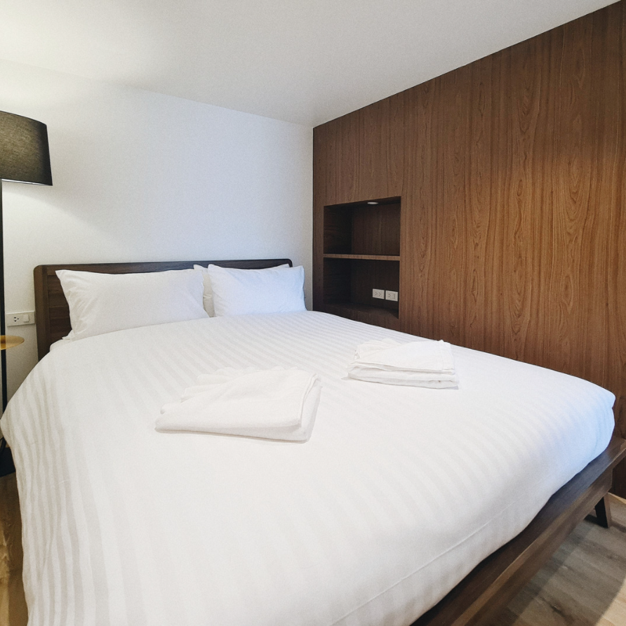 Bedroom with white bedding, wooden headboard, wooden paneling, and a black lamp.