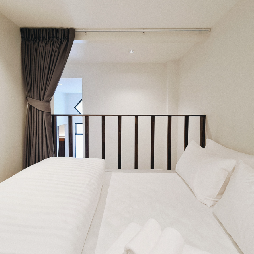 Bedroom with white bedding, gray curtain, and wooden railing.