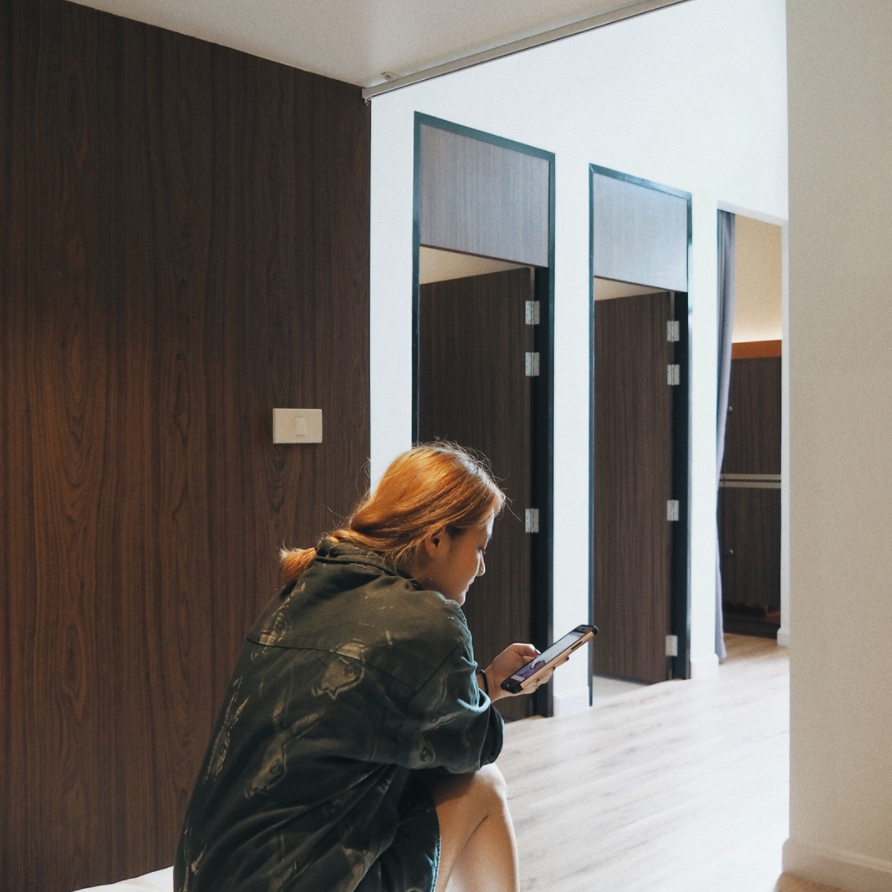 Woman using phone in a hallway with wood-paneled walls and doorways.