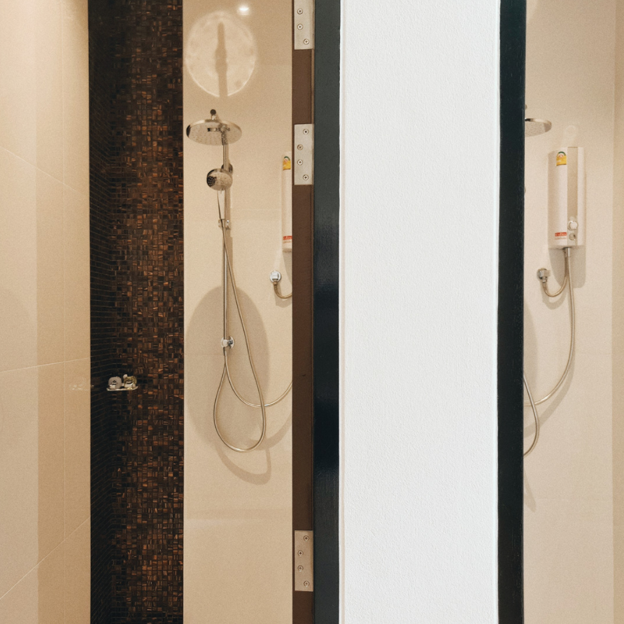 Two shower stalls, one with dark mosaic tile, the other with white wall. Both have shower heads and chrome fixtures.
