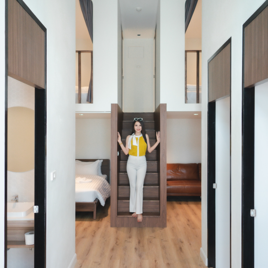 Woman on stairs, hallway with beds, doors, and a leather sofa.