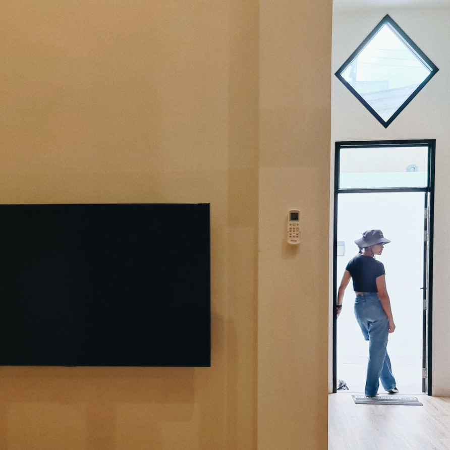Person in a doorway, wearing a hat, looking outside. Interior shot with a flat black panel and a diamond-shaped window.
