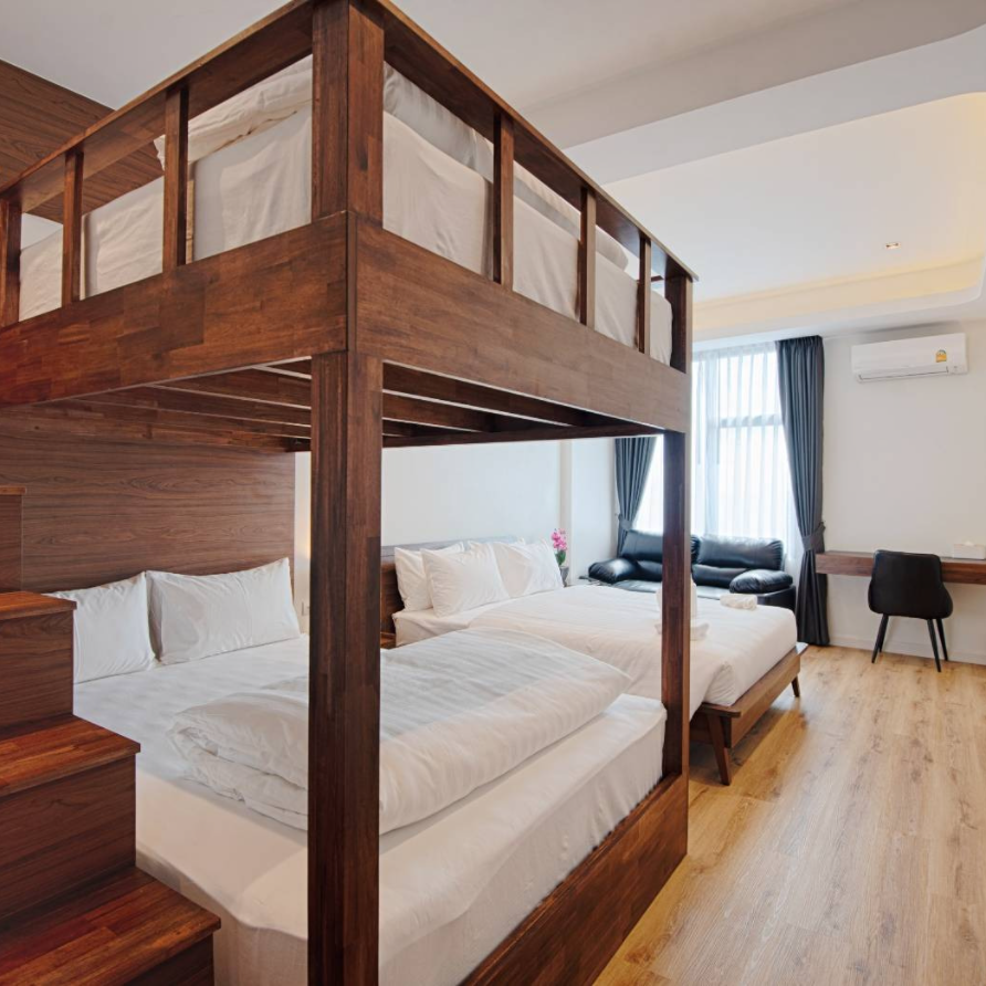 Wooden bunk bed and two beds in a hotel room with desk, black couch, and white linens.