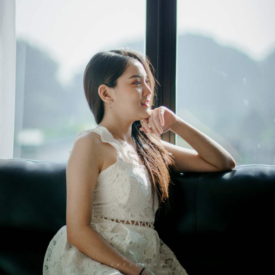 Woman in white dress, smiling, resting arm on sofa, looking out window.
