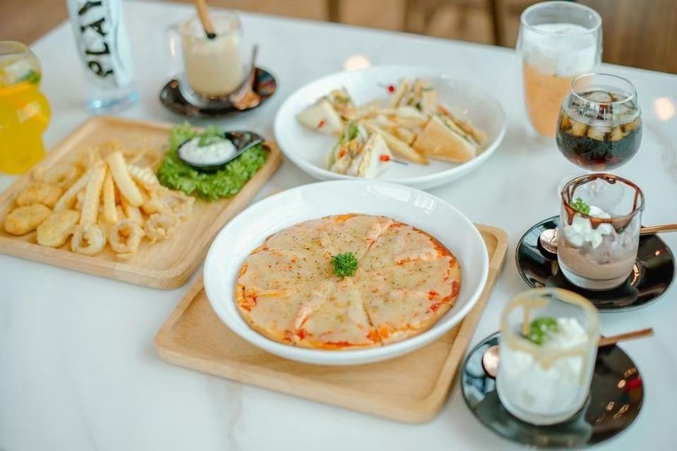Overhead shot of a table with a variety of cafe food and drinks: pizza, sandwiches, fries, beverages, desserts.
