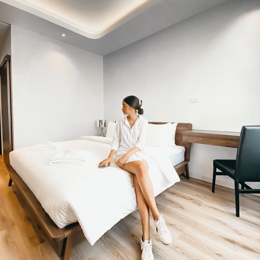 Woman sitting on bed in a modern, light-filled hotel room with a desk.